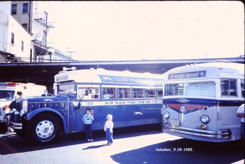 A vintage Greyhound bus and another bus parked in Hoboken, with two children standing nearby, dated September 28, 1985.
