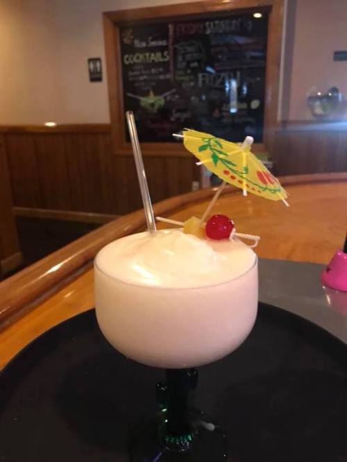 A tropical cocktail in a green glass, topped with a small umbrella, cherry, and pineapple slice.