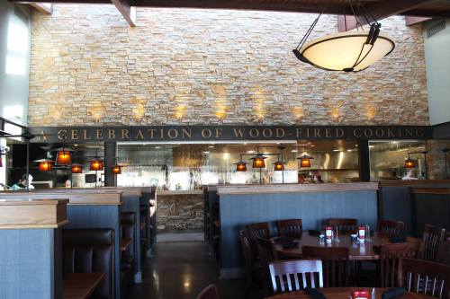 Interior of a restaurant featuring stone walls, wooden booths, and a sign that reads "A Celebration of Wood-Fired Cooking."