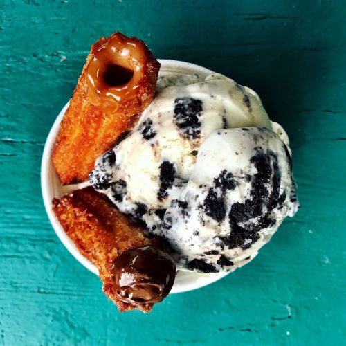 A bowl of cookies and cream ice cream topped with two churros, one filled with caramel and the other with chocolate.