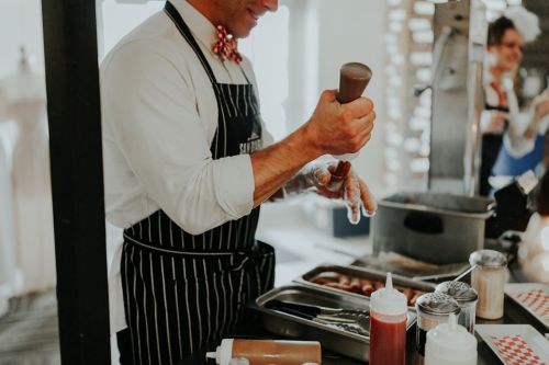 A person in an apron is squeezing sauce from a bottle while preparing food at a counter.