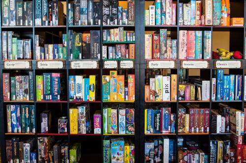 A colorful display of board games organized on shelves, labeled by categories like Co-op, Trivia, and Party.
