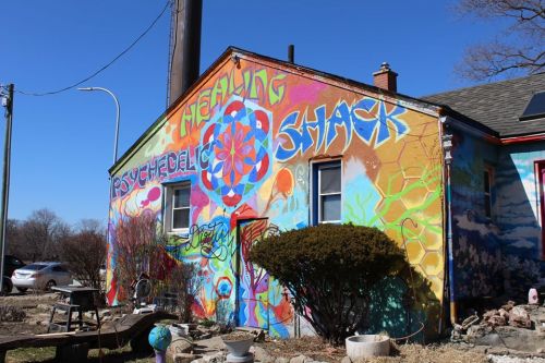 Colorful mural on a house featuring vibrant designs and the words "Healing Shack" and "Psychedelic Shack."