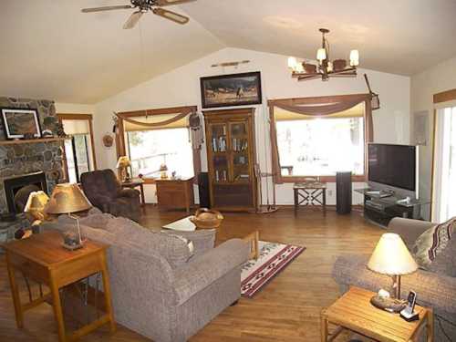 Cozy living room with a stone fireplace, large windows, and comfortable seating, featuring wooden furniture and warm lighting.