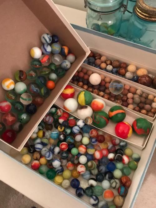 A collection of colorful marbles in a box, featuring various sizes and patterns, arranged neatly.