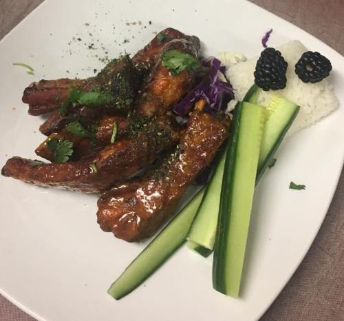 A plate of glazed ribs garnished with herbs, served with rice, cucumber slices, purple cabbage, and blackberries.