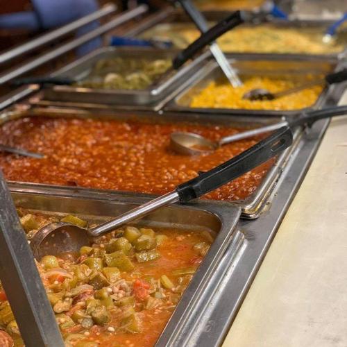 A buffet display featuring various dishes in metal trays, including beans, okra, and a yellow rice dish.