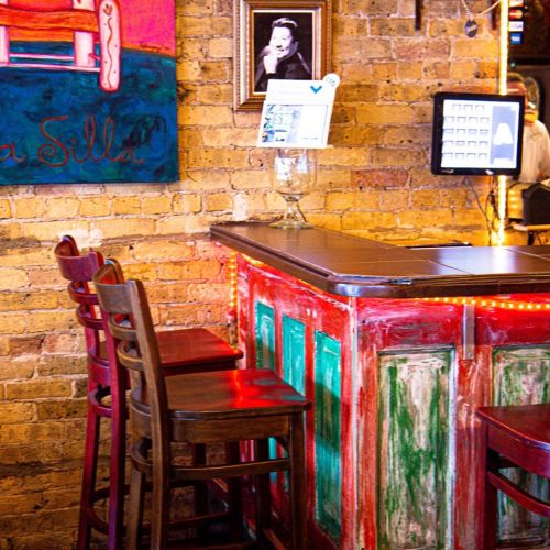 A rustic bar with colorful paint, wooden stools, and a framed photo on the wall in a cozy setting.