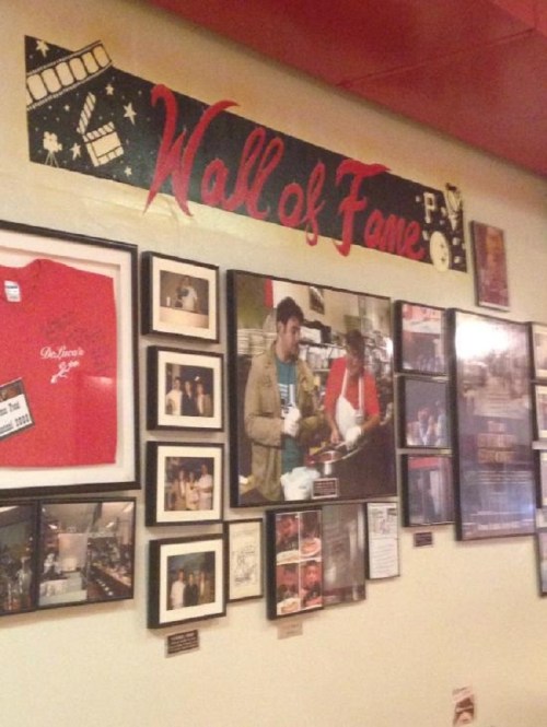A restaurant's "Wall of Fame" featuring framed photos and memorabilia, including a red shirt and celebrity images.