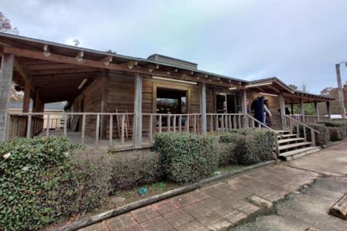 A wooden building with a porch and steps, surrounded by hedges, under a cloudy sky.
