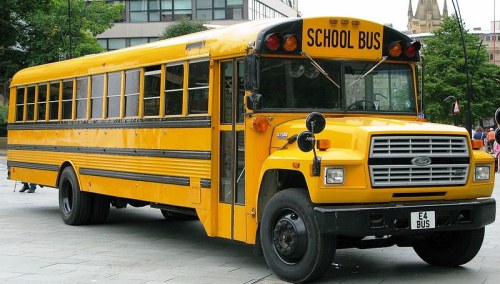 A yellow school bus parked on a city street, with large windows and a sign reading "SCHOOL BUS" on the front.