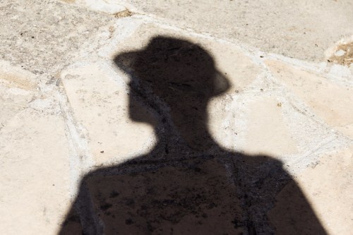 A shadow of a person wearing a hat cast on a stone surface.