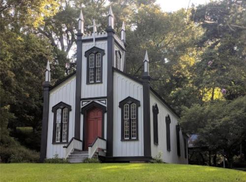 A quaint, Gothic-style church with a red door and spires, surrounded by lush greenery.