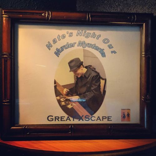 A framed poster for "Nate's Night Out Murder Mysteries" featuring a person in a trench coat at a table.