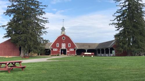 A red barn with a cupola, surrounded by green grass and tall trees, under a partly cloudy sky.