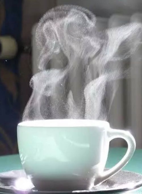 A steaming cup of coffee or tea on a table, with wisps of steam rising into the air.