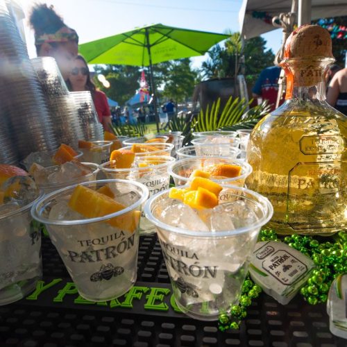A table with cups of ice and orange slices, featuring a bottle of Patrón tequila and festive decorations.