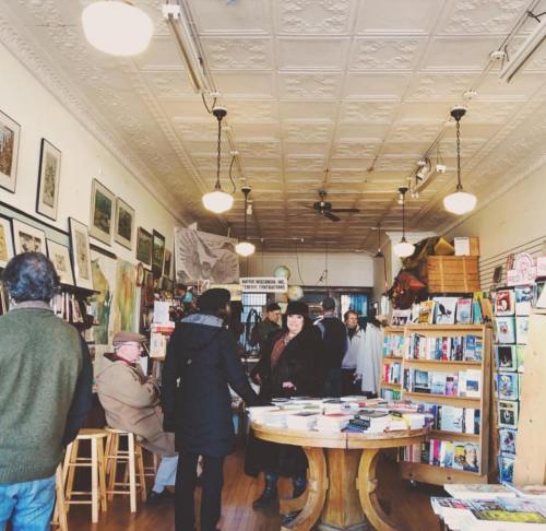 A cozy bookstore interior with people browsing books, art on the walls, and a warm, inviting atmosphere.