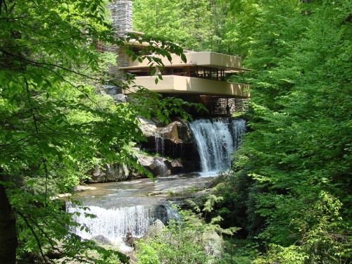 A modern house nestled among lush greenery, overlooking cascading waterfalls in a serene forest setting.