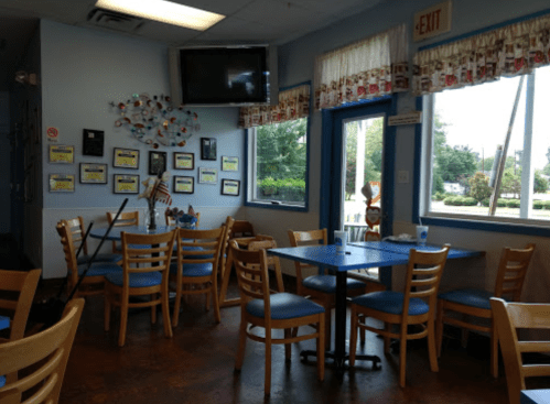 A cozy restaurant interior with blue tables, wooden chairs, and wall decorations, including framed photos and a TV.