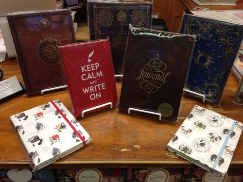 A display of various decorative journals and notebooks on a wooden table, featuring different designs and colors.