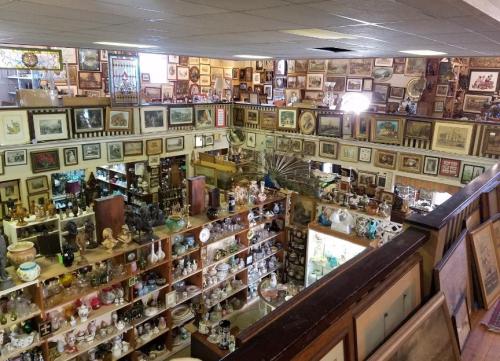 A spacious antique shop filled with shelves of collectibles, framed art, and various decorative items.