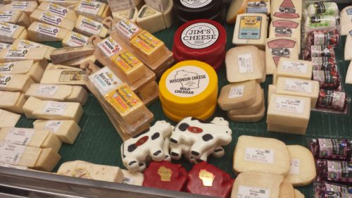 A variety of cheeses displayed on a green surface, including blocks, rounds, and cow-shaped cheese.