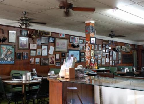 A cozy diner interior with wooden walls adorned with framed photos and memorabilia, featuring green seating and a counter.