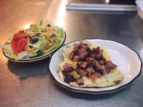 A plate with chopped steak on a baked potato, served with a side salad of lettuce, tomatoes, and cheese.