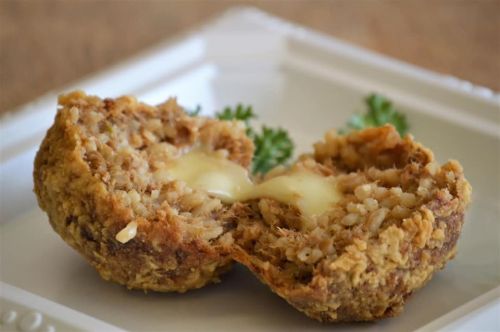 A golden-brown, crispy ball cut in half, revealing melted cheese inside, garnished with parsley on a white plate.