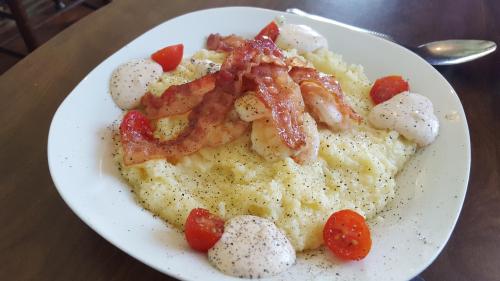 A plate of creamy grits topped with crispy bacon, cherry tomatoes, and dollops of sauce, garnished with black pepper.