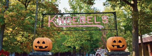 Sign for Knoebels amusement park with Halloween-themed pumpkins on either side, surrounded by colorful autumn trees.