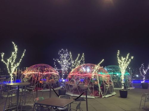 Colorful illuminated igloos surrounded by glowing trees at night, creating a festive outdoor dining atmosphere.