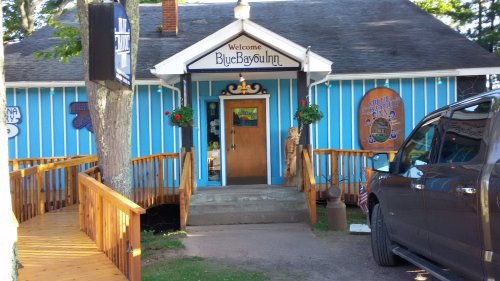 A blue building with a welcoming sign, wooden steps, and a parked vehicle outside.