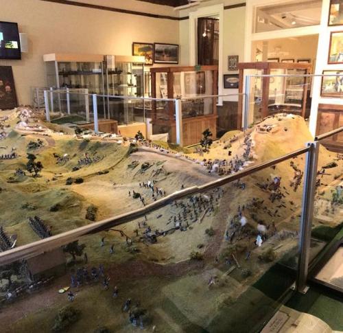 A detailed model depicting a historical battle scene, featuring miniature soldiers and terrain in a museum setting.