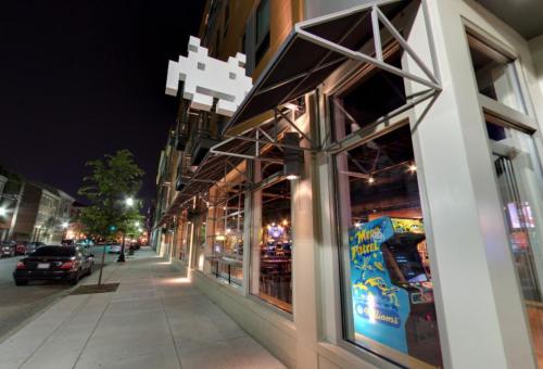 A nighttime street view of a building with arcade-themed decor and an iconic pixelated character above the entrance.
