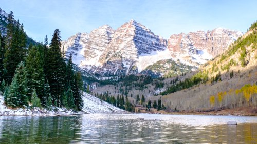 A serene lake surrounded by snow-capped mountains and evergreen trees, reflecting the clear blue sky.