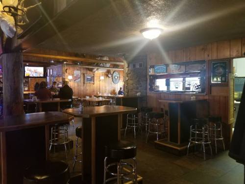 Cozy bar interior with wooden walls, stools, and a TV, featuring a warm, inviting atmosphere.