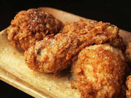 Golden-brown fried chicken pieces on a wooden plate, sprinkled with salt.