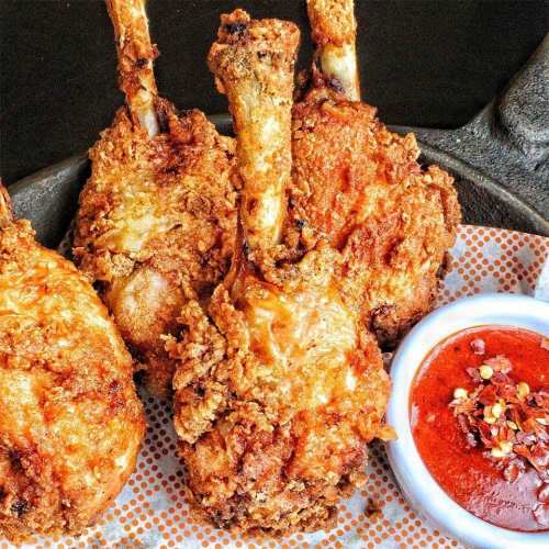 Crispy fried chicken drumsticks served with a side of spicy dipping sauce on a patterned plate.