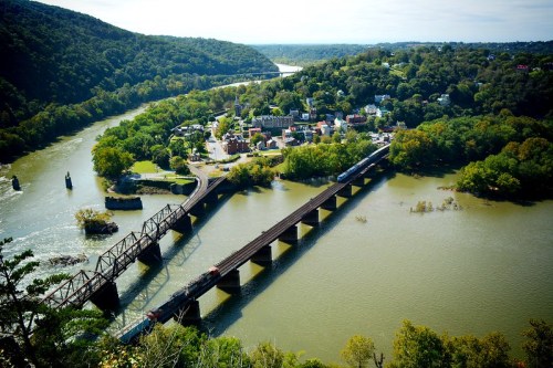 Aerial view of a river winding through green hills, with a town and a train bridge crossing the water.