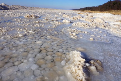 A frozen landscape with large, round ice formations scattered across a reflective surface under a clear blue sky.