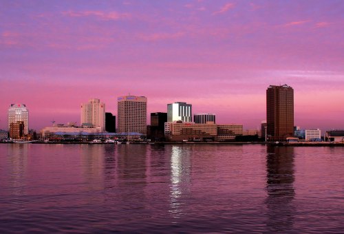 City skyline at sunset, reflecting on water with pink and purple hues in the sky.