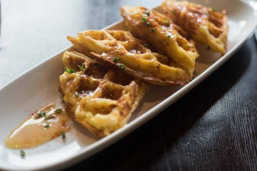 A plate of golden-brown waffles drizzled with syrup and garnished with green onions.