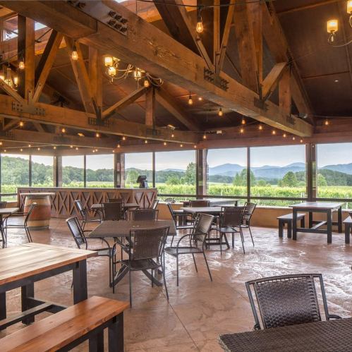 A spacious, rustic venue with wooden beams, tables, and a scenic view of mountains through large windows.