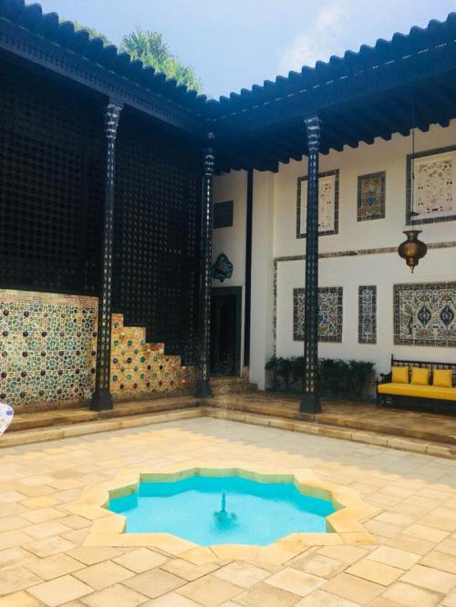 A courtyard with a blue fountain, intricate tile work, and decorative pillars under a bright sky.