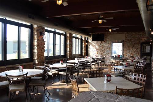 Bright restaurant interior with stone walls, large windows, and empty tables set for dining.
