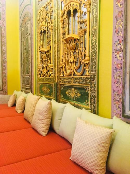 A vibrant room with ornate golden wall decor and a cozy orange seating area adorned with patterned cushions.