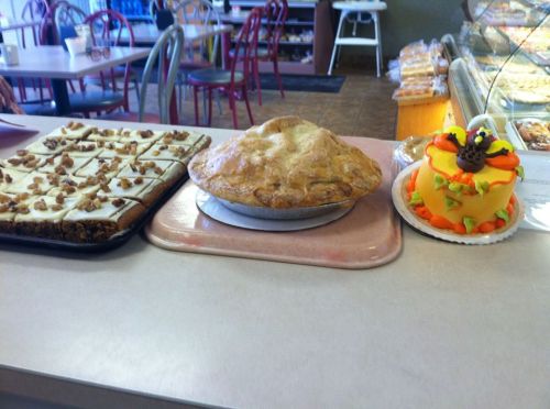A display of three desserts: a tray of frosted bars, a golden pie, and a colorful cake decorated for a celebration.