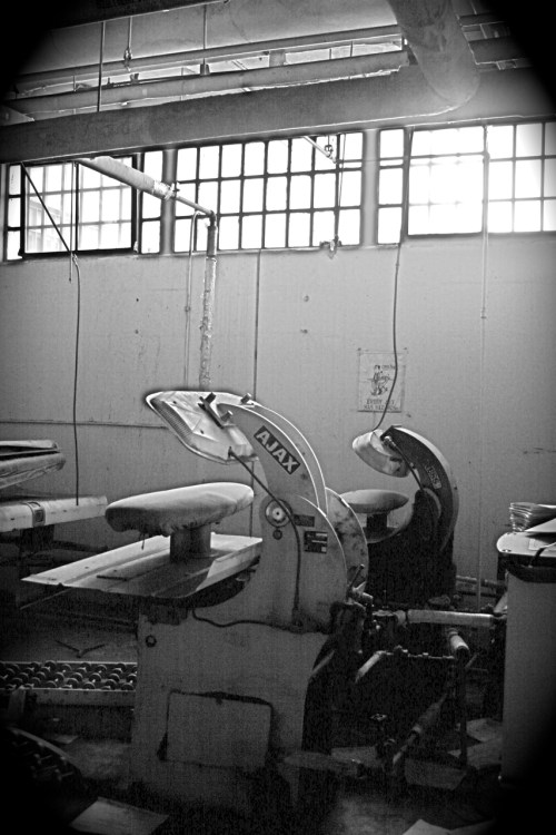 Black and white image of industrial sewing machines in a workshop, with large windows in the background.